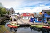 Una orilla con edificios de colores, un muelle y kayaks.