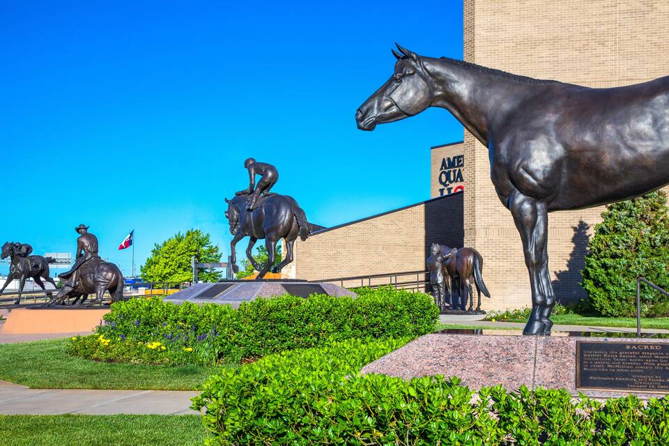 Une série de statues de chevaux dans un parc, avec un bâtiment en arrière-plan.