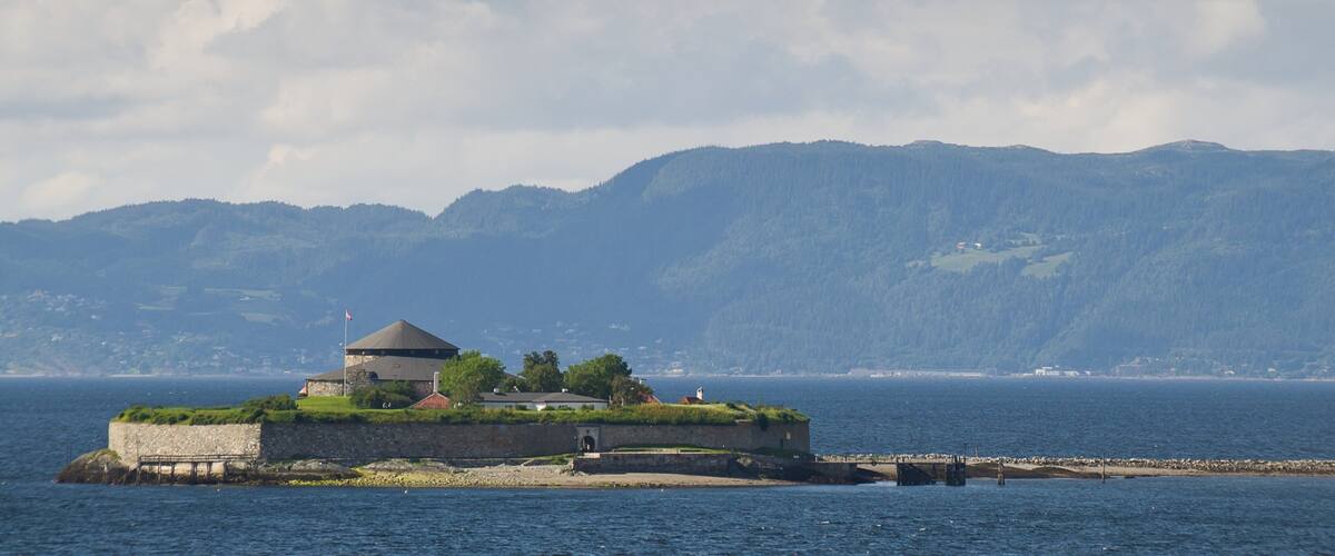 A coastal fort with a turret, surrounded by water and mountains in the background.