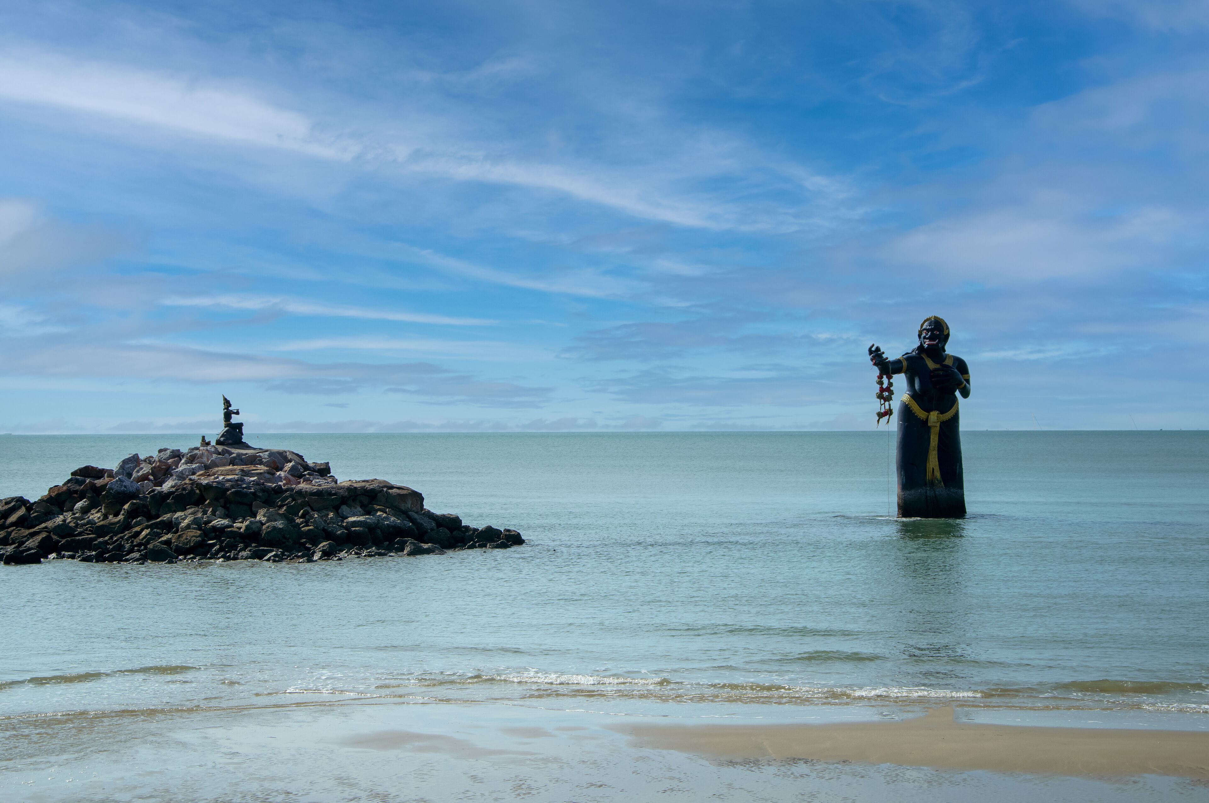 A statue in a body of water with a rocky outcrop in the background.