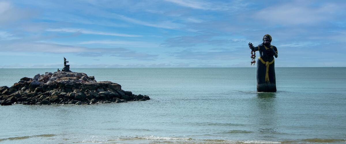 A statue in a body of water with a rocky outcrop in the background.