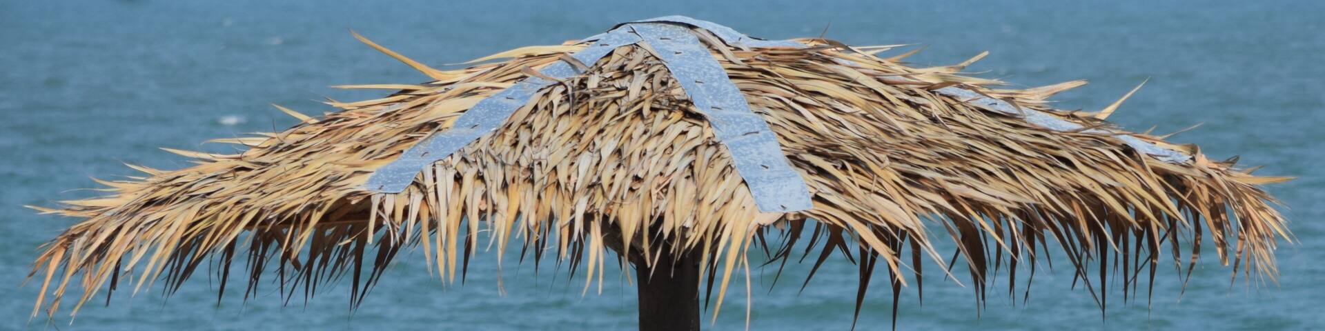 A beach umbrella with a thatched roof and a wooden bench.