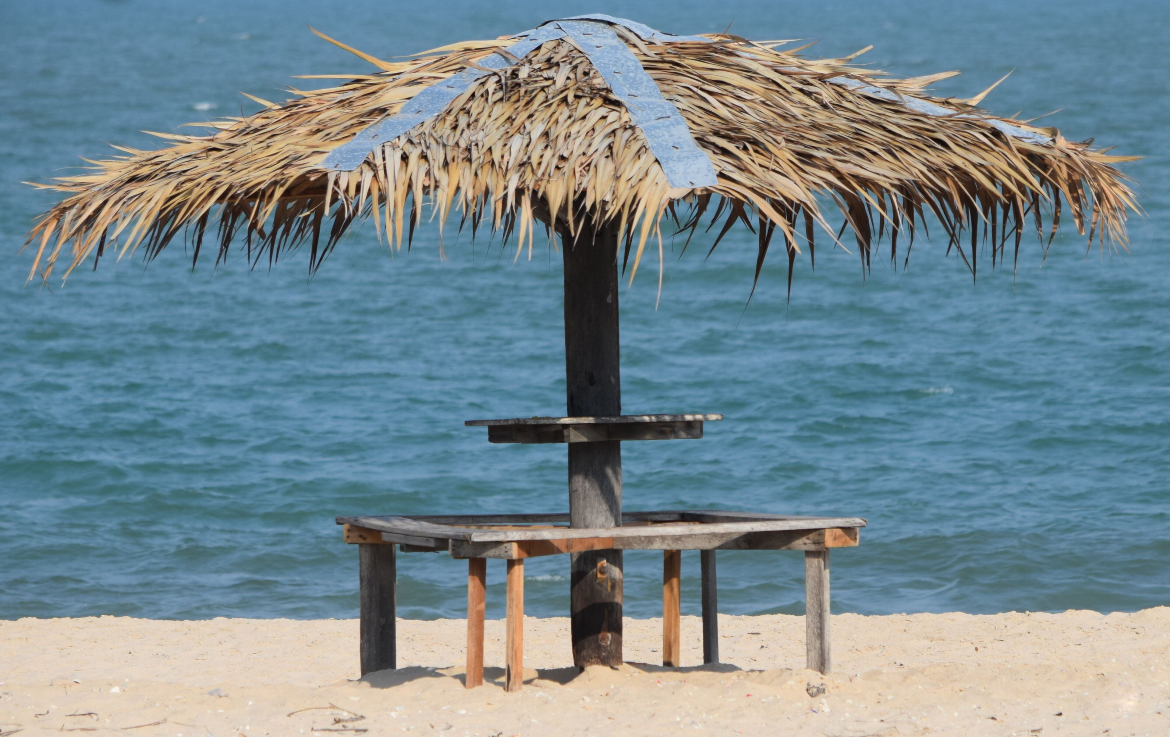 A beach umbrella with a thatched roof and a wooden bench.