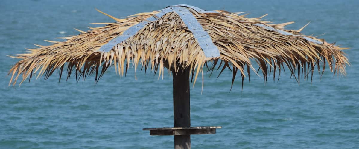 A beach umbrella with a thatched roof and a wooden bench.