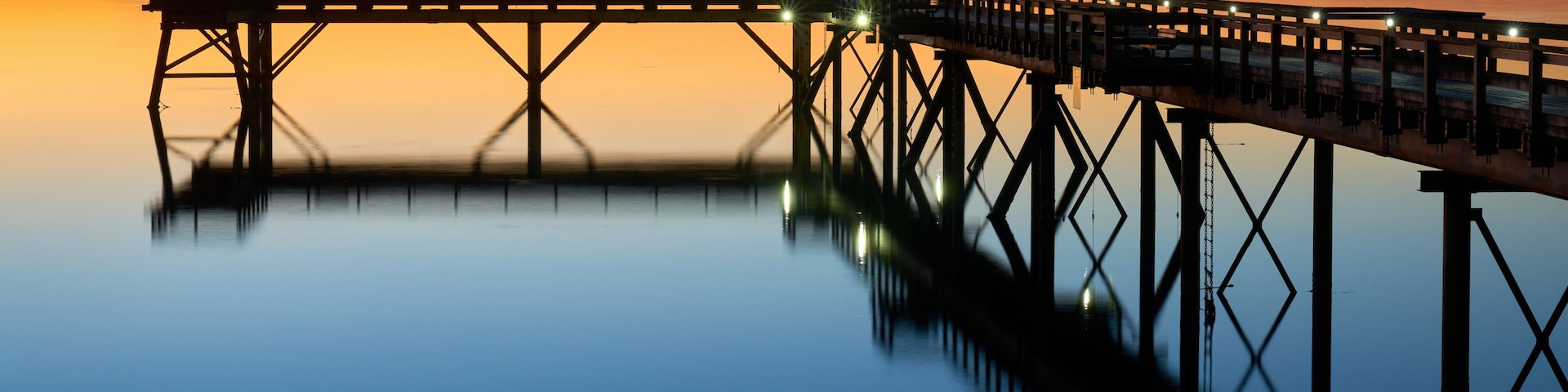 Un muelle que se adentra en aguas tranquilas, con un atardecer de fondo.