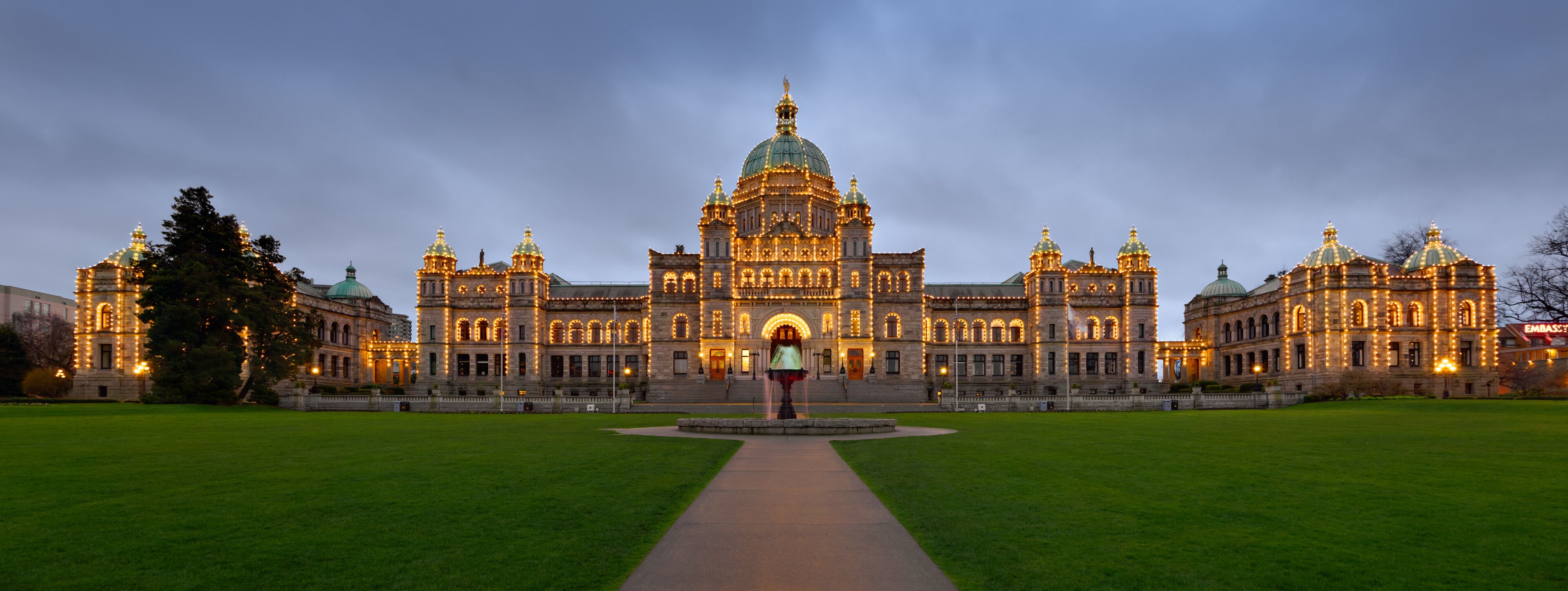 A grand, illuminated building with domed architecture, a central fountain, and a well-maintained lawn.