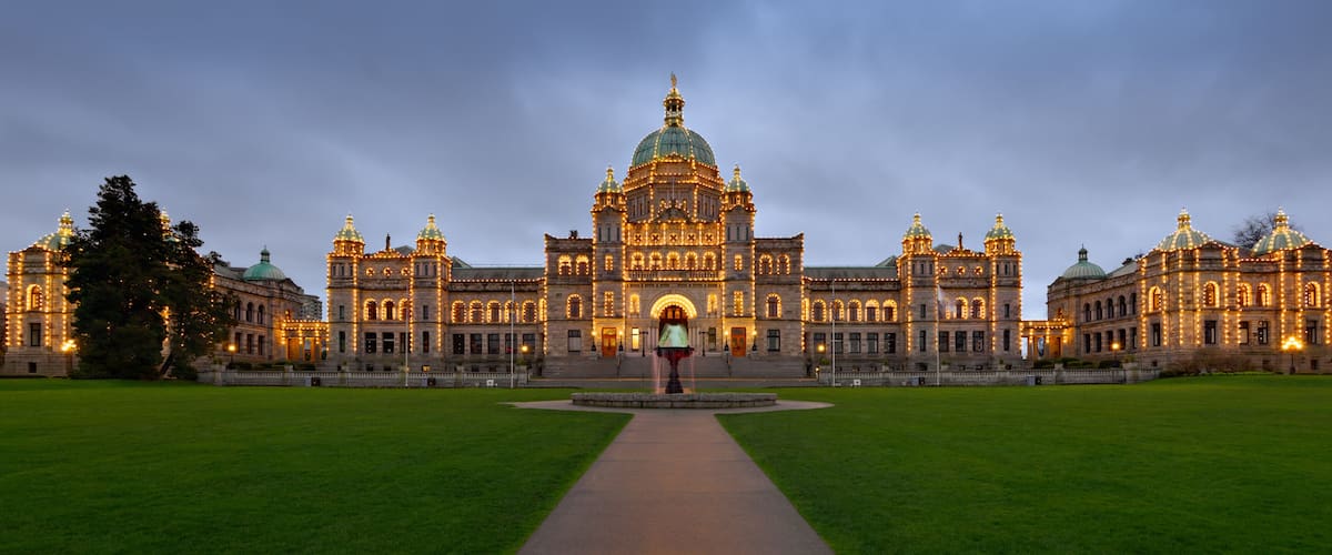 A grand, illuminated building with domed architecture, a central fountain, and a well-maintained lawn.