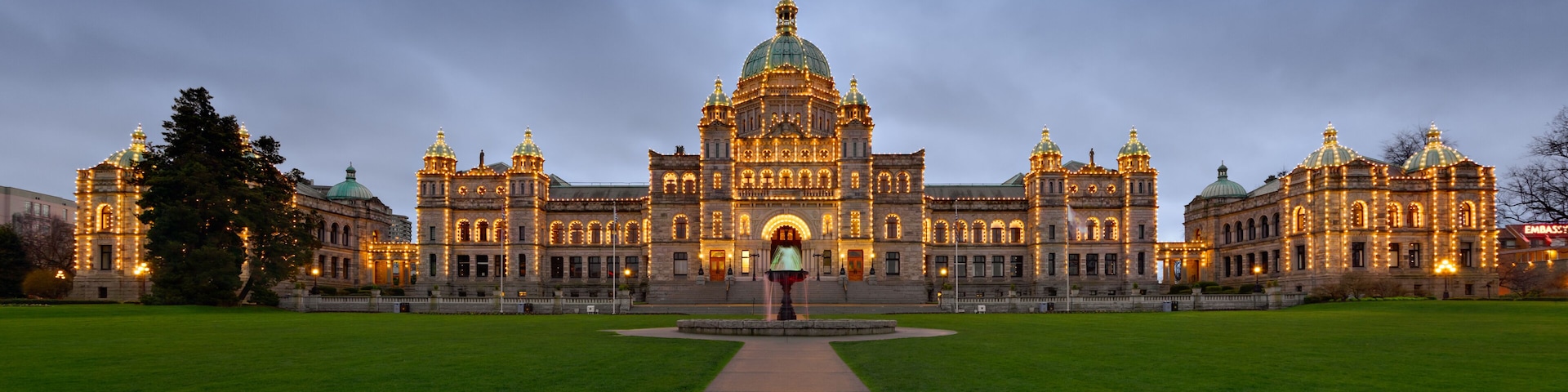 A grand, illuminated building with domed architecture, a central fountain, and a well-maintained lawn.