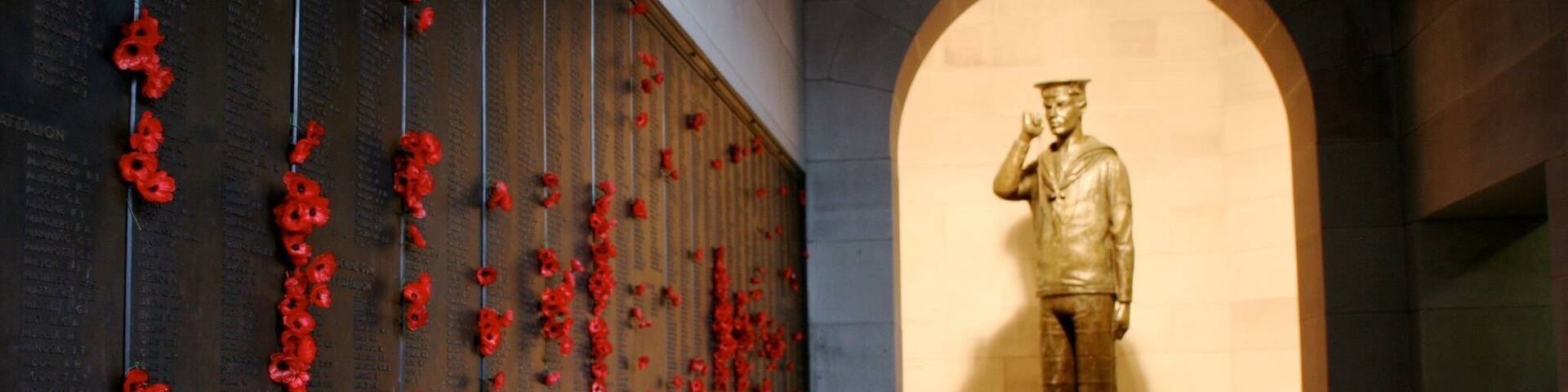 A memorial wall with red poppies and a statue of a man in a suit.