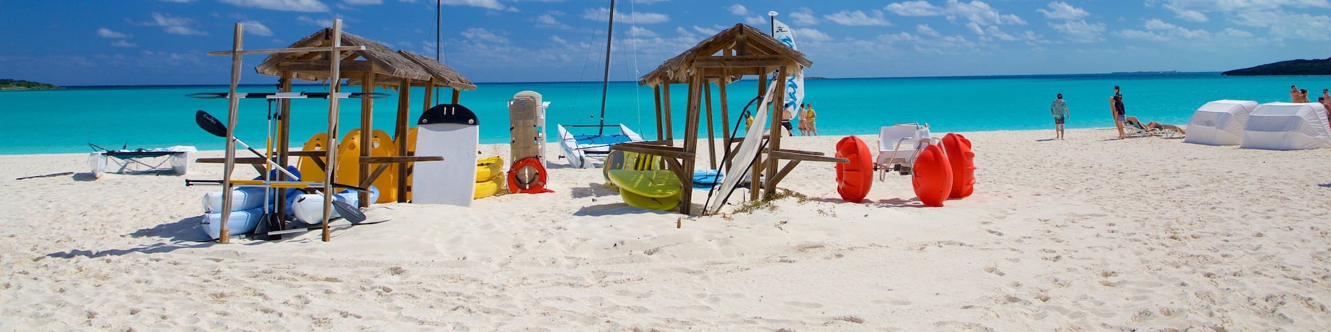 A beach with clear turquoise water, two wooden gazebos, and various beach equipment.