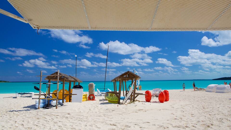 A beach with clear turquoise water, two wooden gazebos, and various beach equipment.