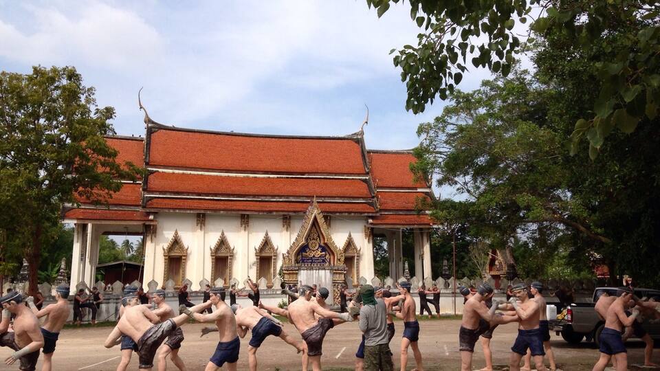 A group of people practicing martial arts in front of a temple with a traditional red roof.