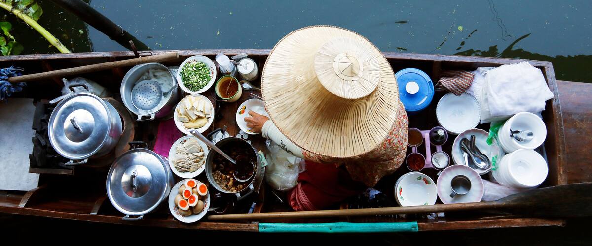 A wooden boat filled with cooking utensils, pots, and food items, floating on water.