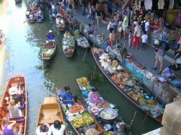 A bustling riverside market with numerous boats filled with goods and people.