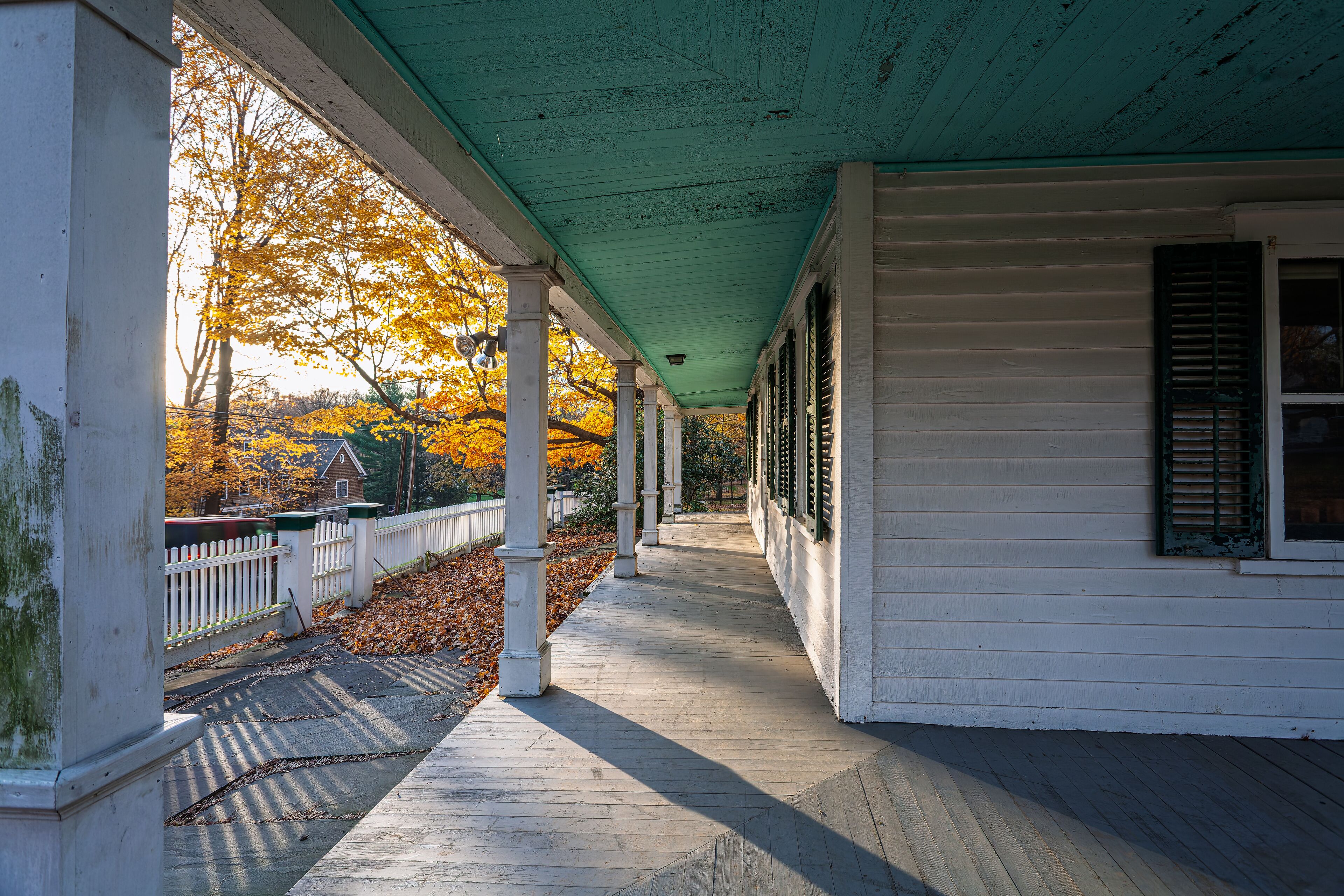 Sunlit view of Ambler Farm porch with autumn foliage in Wilton CT