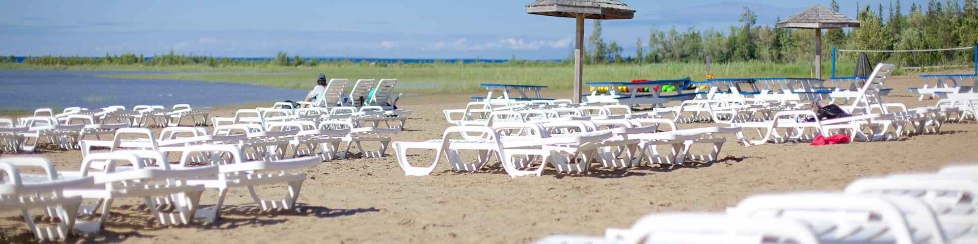 A beach with rows of white lounge chairs and thatched umbrellas.