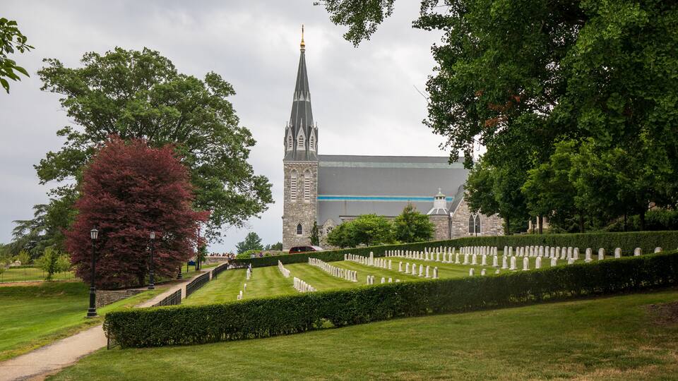 A cemetery with neatly trimmed hedges and a church with a tall steeple in the background.