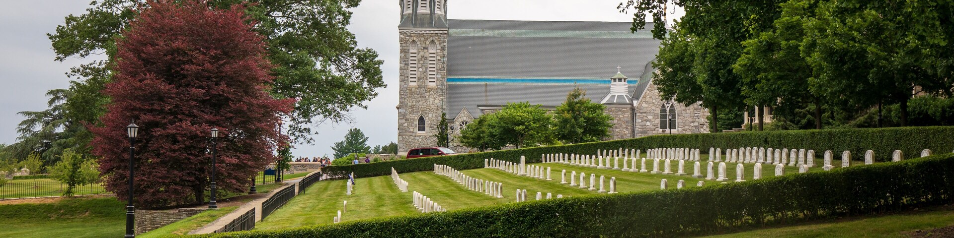 Un cementerio con setos bien cuidados y una iglesia con un campanario alto al fondo.