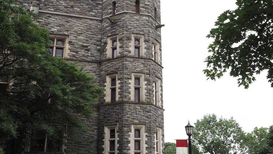 A stone castle-like building with a turret, surrounded by trees and a pathway.