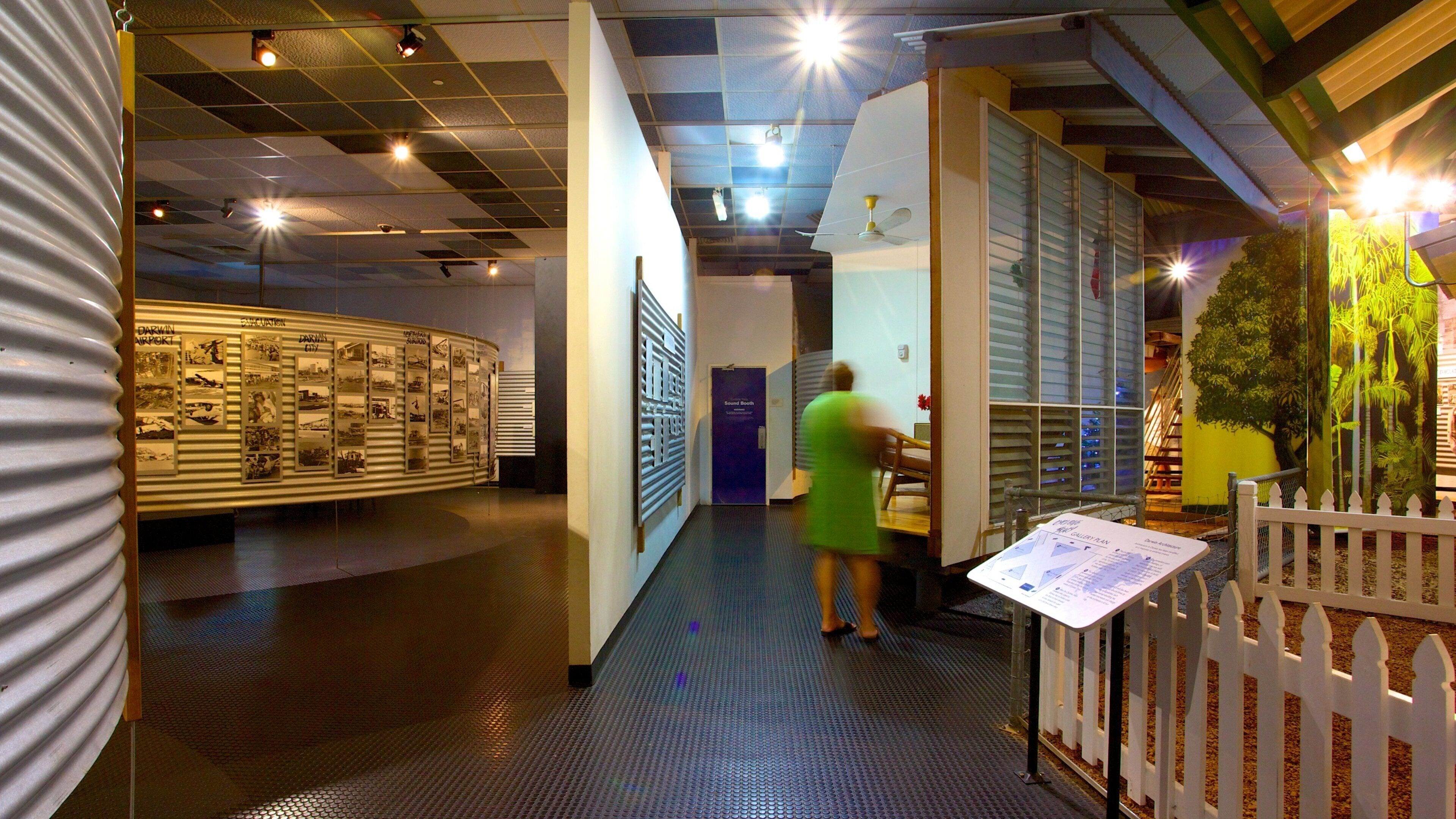 Um corredor de museu com exposições, uma cabine de som e uma vitrine com plantas tropicais.