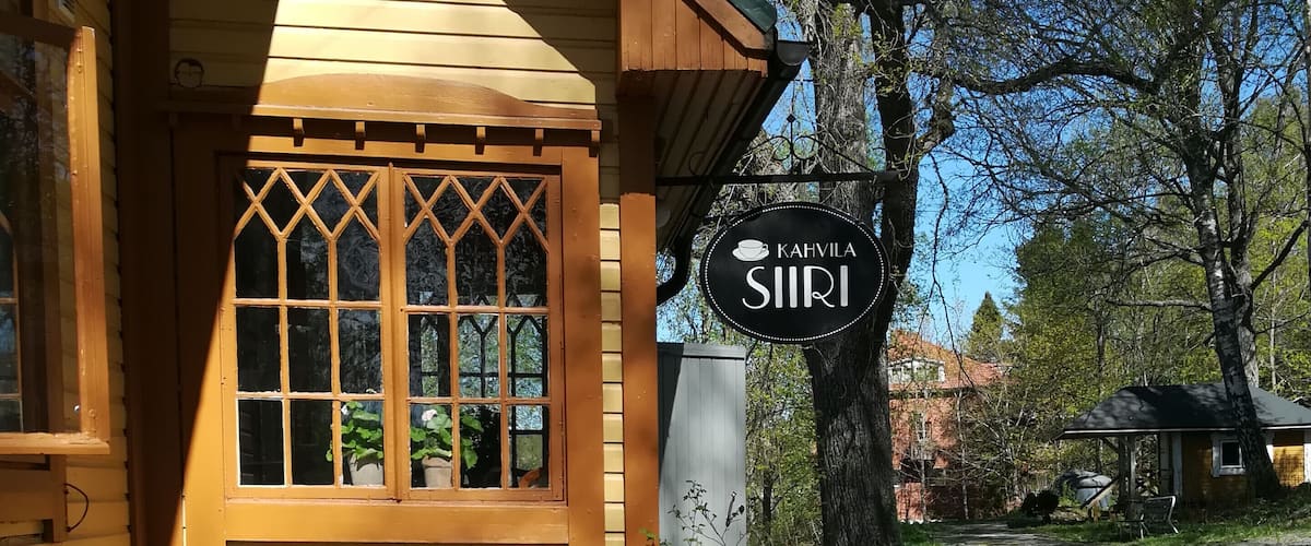 A wooden cabin with a sign reading "Kahvilasiiri" and outdoor seating.