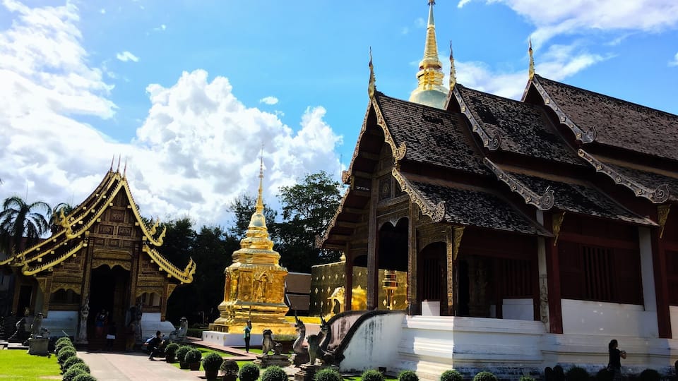 A traditional temple complex with ornate golden structures and a white building with a tiled roof.