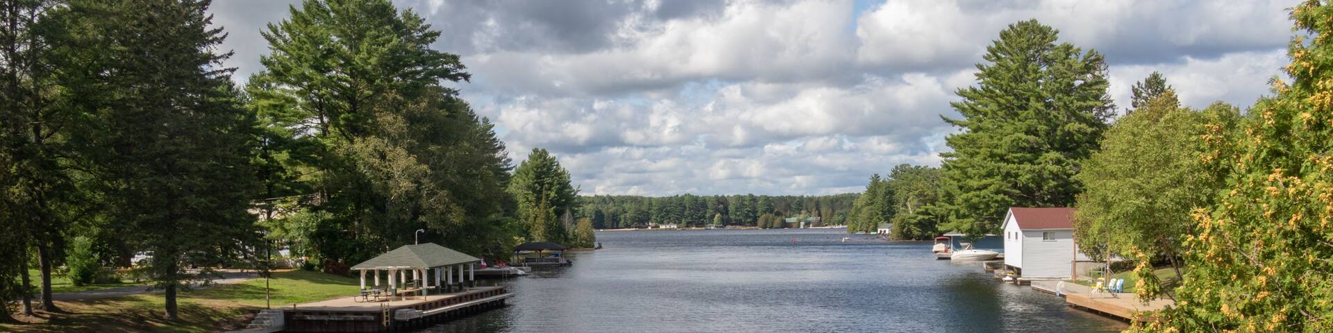 A calm river with a gazebo and a small house on the left bank, surrounded by dense trees.