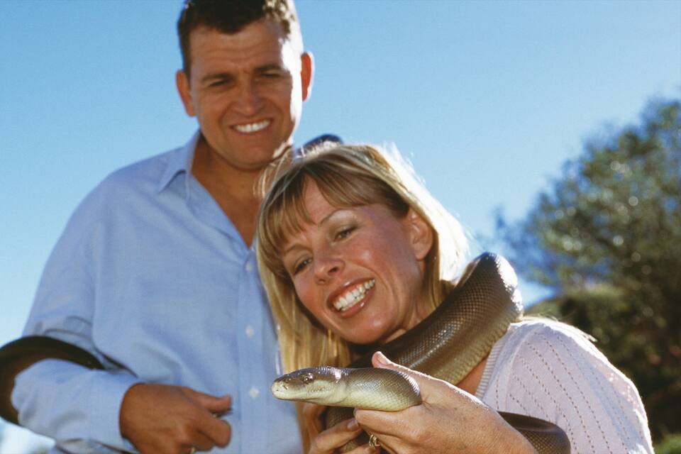 A person holding a snake outdoors with a clear blue sky in the background.