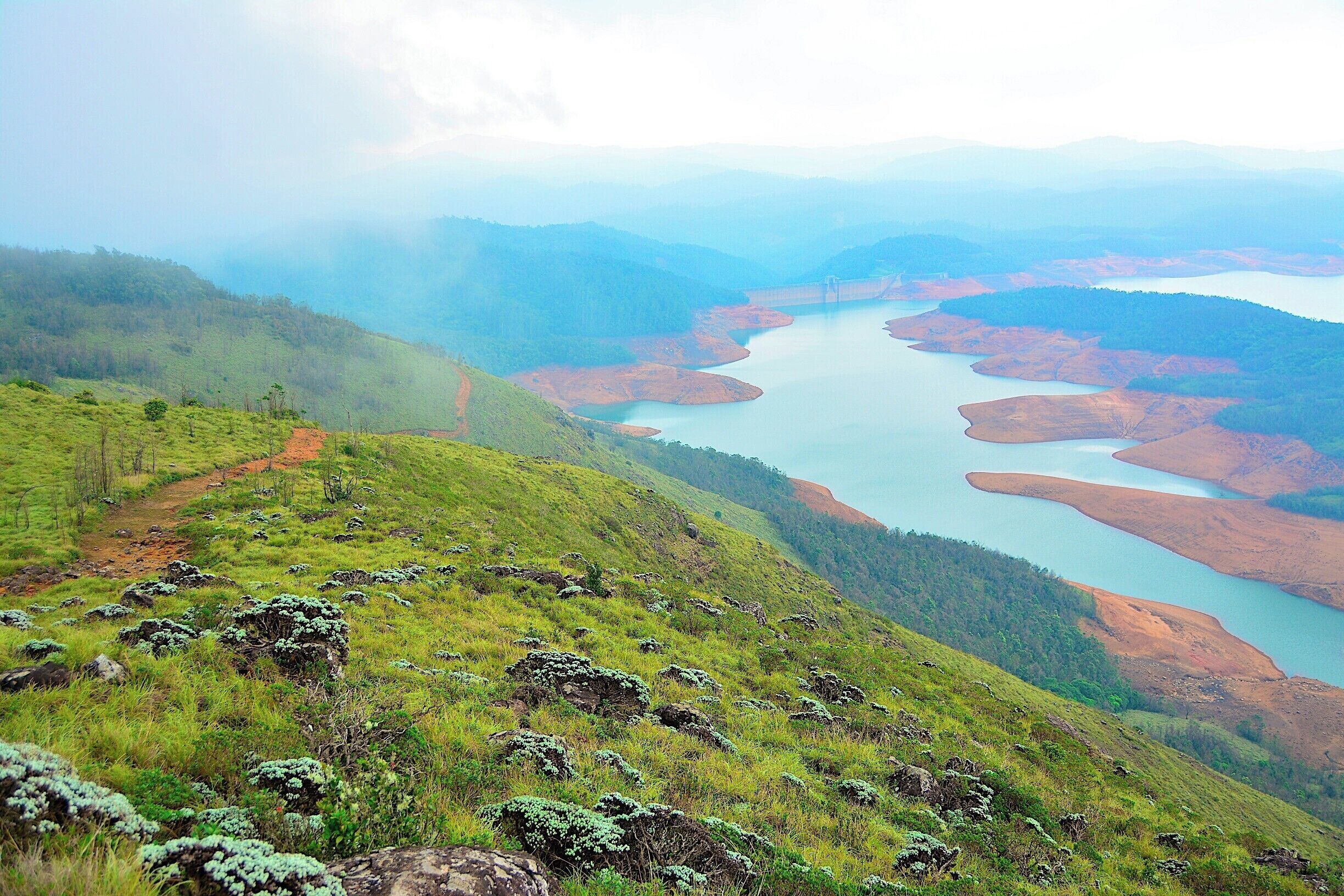 A river winding through a hilly landscape with patches of red earth and green vegetation.