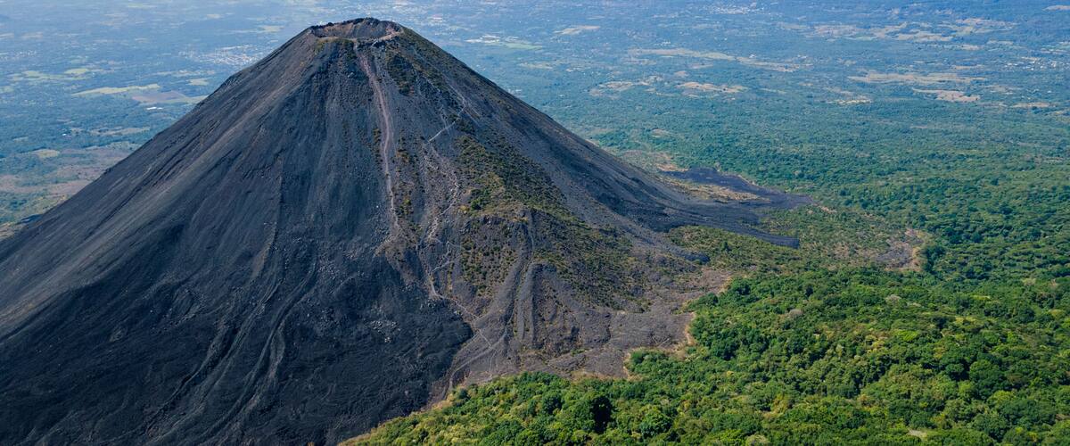 A volcanic mountain with a distinct peak and surrounding forested area.