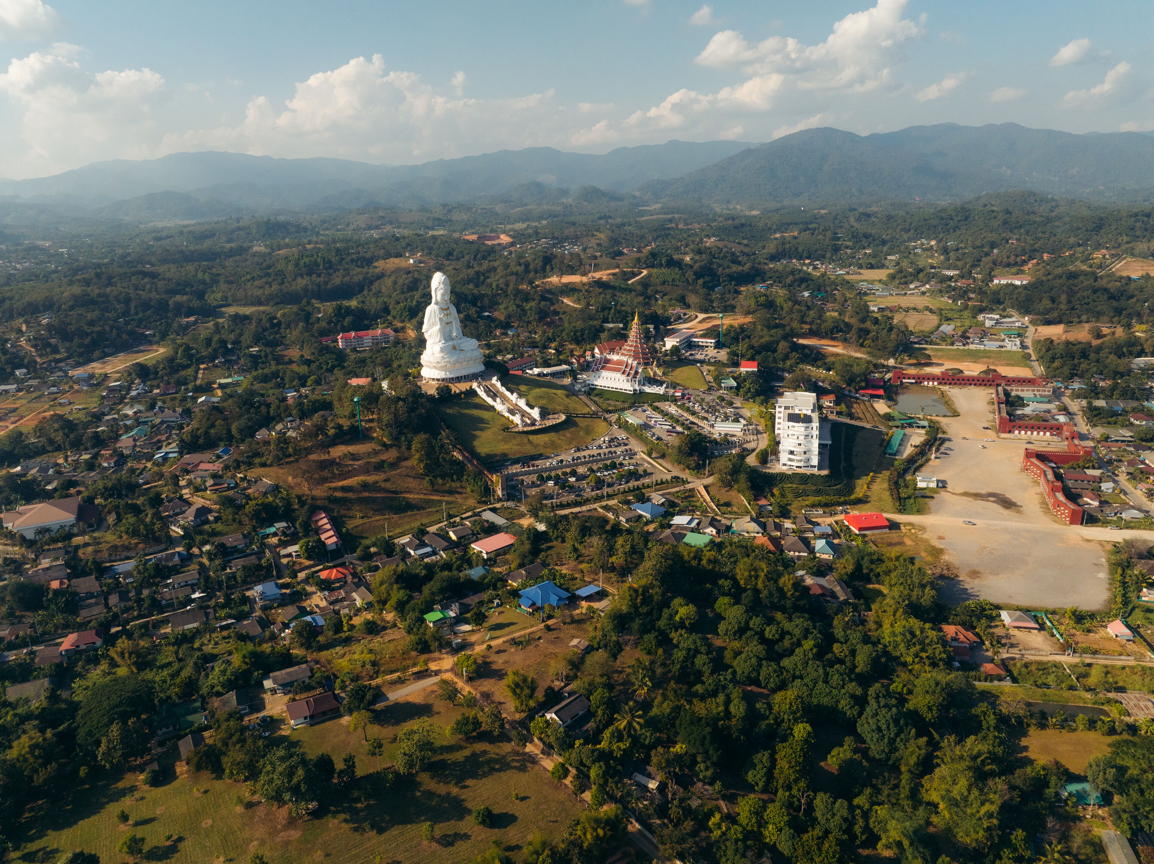 Aerial view of the serene Guan Yin statue standing tall amidst the tranquil landscape, a spiritual beacon under the vast sky, Tambon Ban Du, Chang Wat Chiang Rai, Thailand.