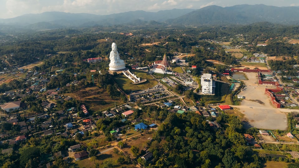 An aerial view of a town with a large white statue, a pagoda, and surrounding greenery.
