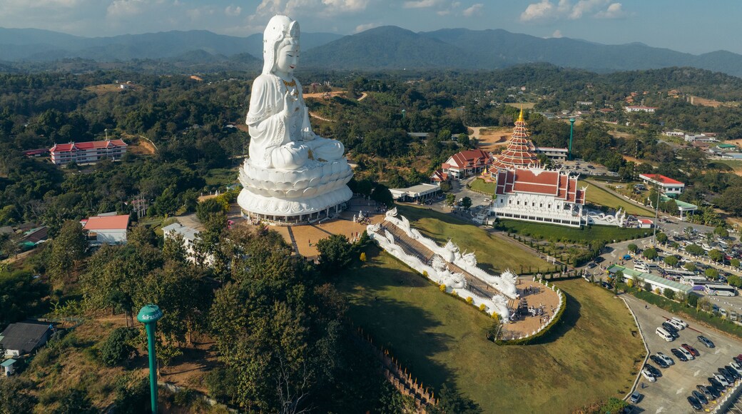 Aerial view of a majestic white Guan Yin statue stands serenely amidst lush greenery and traditional Thai architecture, Guan Yin Statue, Chang Wat Chiang Rai, Thailand.