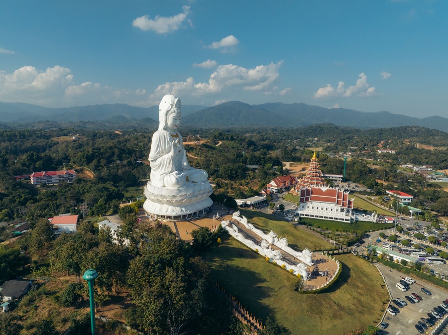 Aerial view of a majestic white Guan Yin statue stands serenely amidst lush greenery and traditional Thai architecture, Guan Yin Statue, Chang Wat Chiang Rai, Thailand.