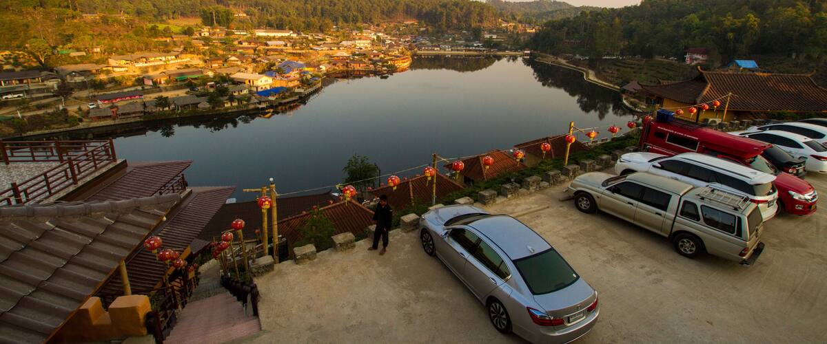 A serene lakeside village with traditional architecture, a parked car, and a red lantern-adorned pathway.