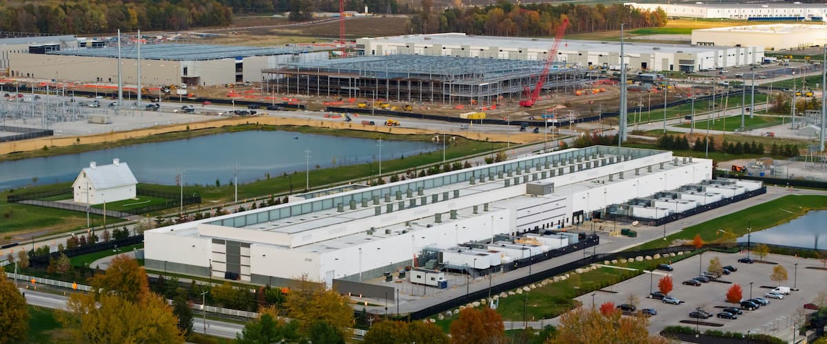 A large industrial complex with multiple buildings, a parking lot, and a small lake.