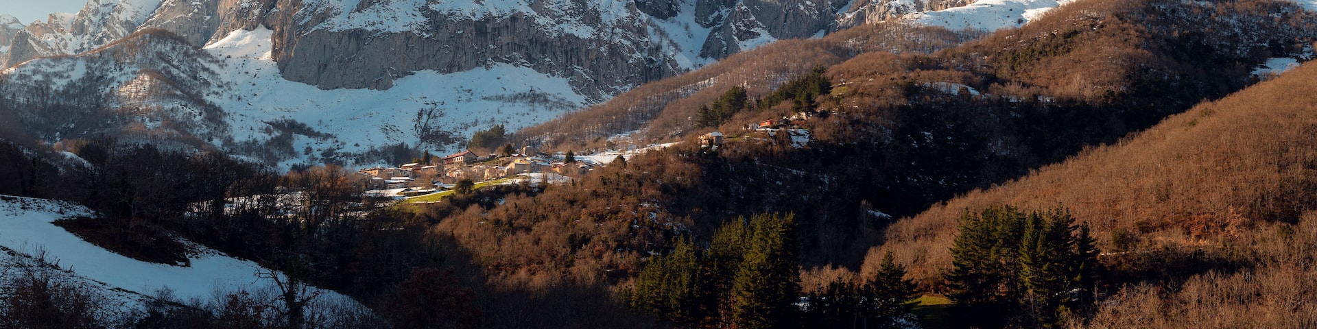 Snow-covered mountains, a valley with buildings, and a lake.