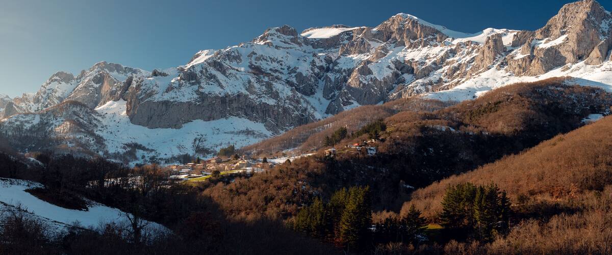Snow-covered mountains, a valley with buildings, and a lake.