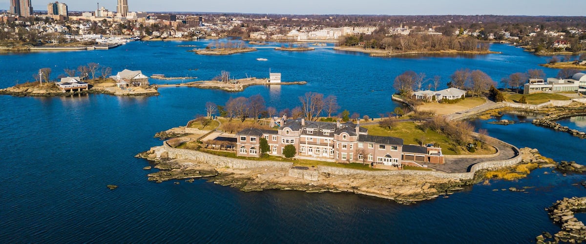 A river with multiple islands, a large estate on the main island, and a city skyline in the background.