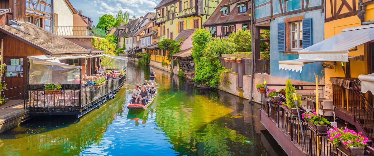 A narrow canal with a boat carrying passengers, surrounded by colorful half-timbered houses.