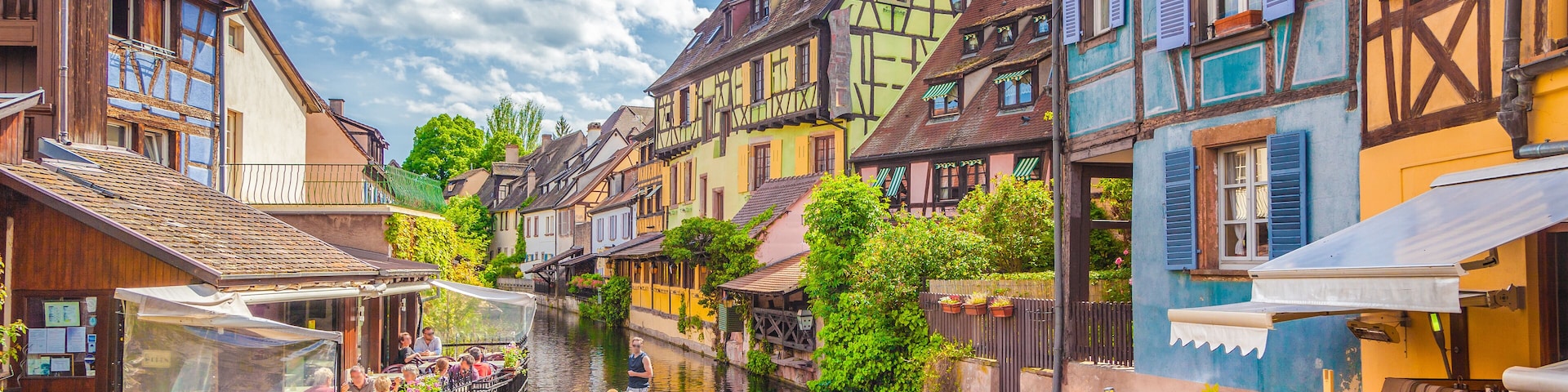 A narrow canal with a boat carrying passengers, surrounded by colorful half-timbered houses.