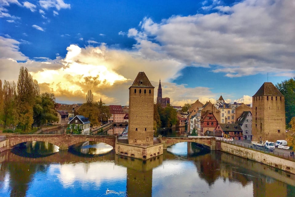 A river with bridges, historic buildings, and a tower reflecting in the water.