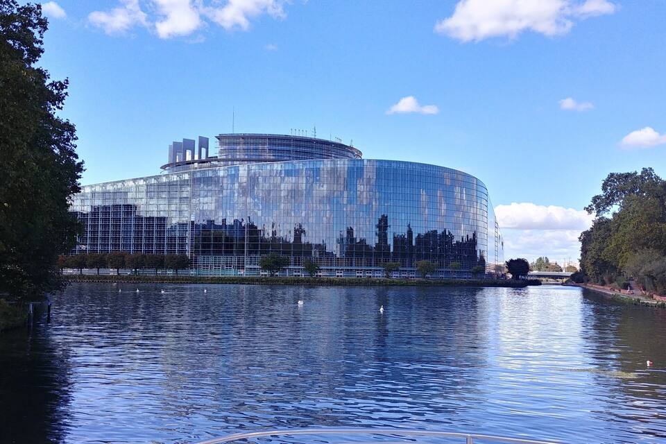 Un bâtiment moderne en verre, situé au bord d’une rivière paisible où nagent des cygnes.