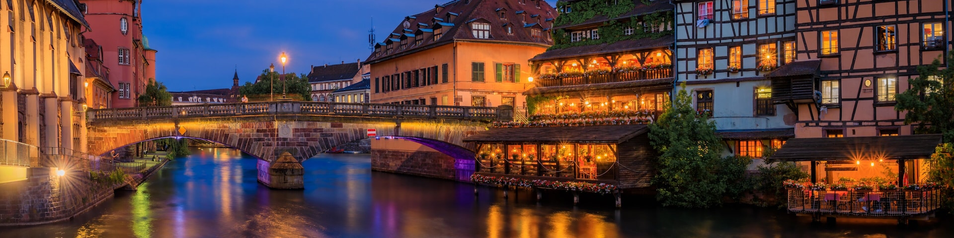 A river with a bridge, illuminated buildings, and a traditional half-timbered house.