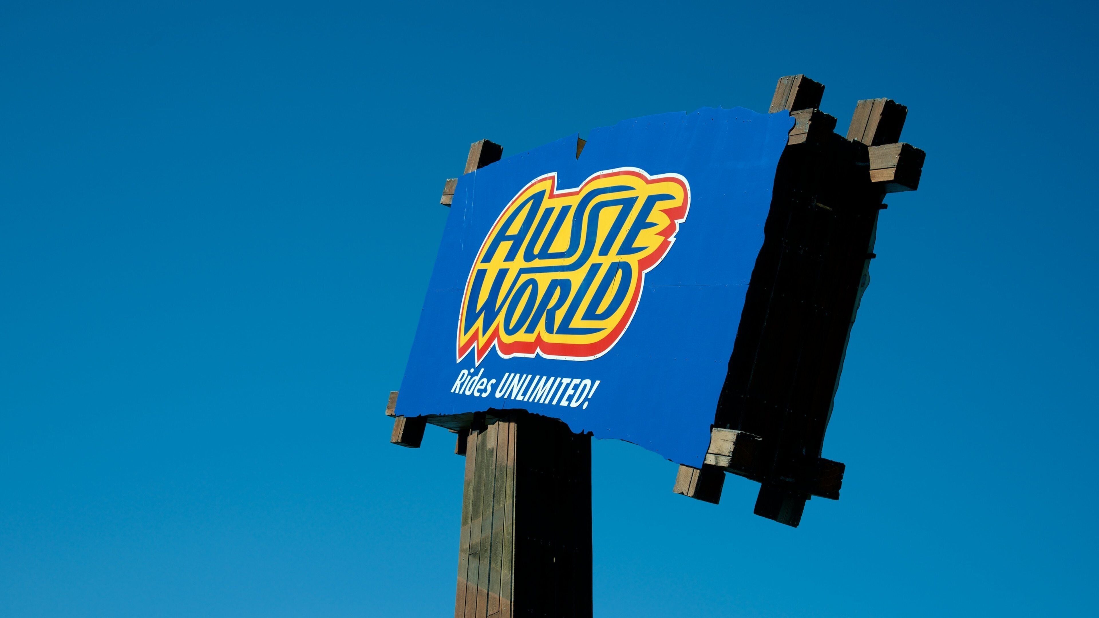 A blue sign with the text "Austie World" and "Rides Unlimited!" against a clear blue sky.