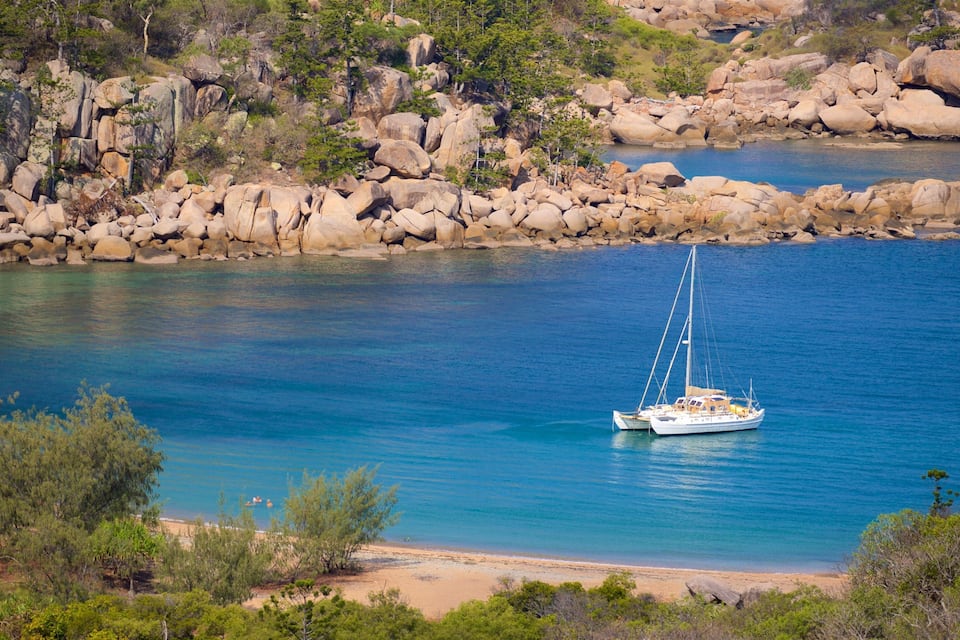 A white sailboat on a turquoise sea with rocky shores and green vegetation.
