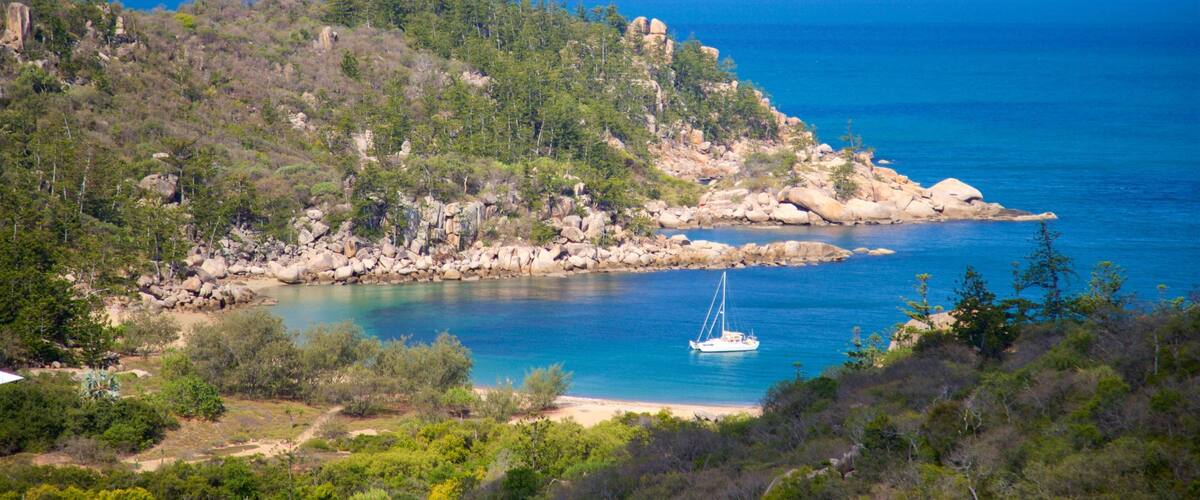 A coastal landscape with a rocky shoreline, a sailboat, and dense green vegetation.