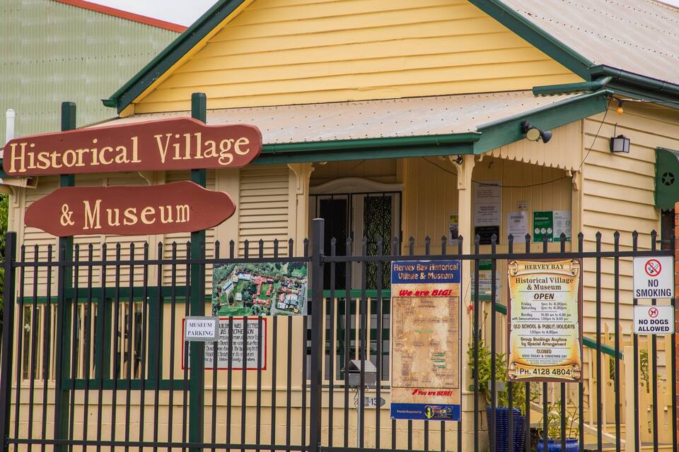 A historical village and museum with a signboard, a fence, and various informational posters.