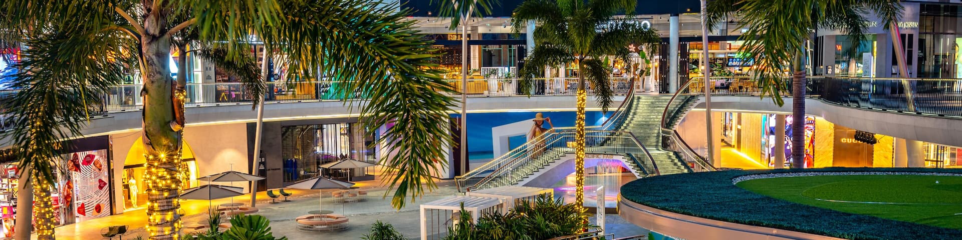 A nighttime view of a modern indoor complex with a swimming pool, palm trees, and a sports field.
