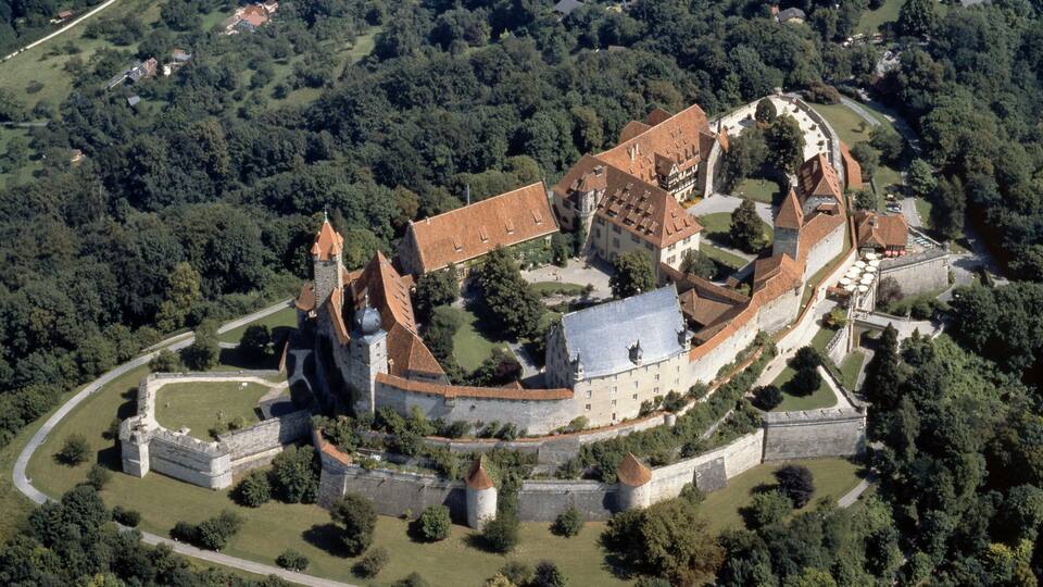 An aerial view of a historic castle complex surrounded by dense forest.